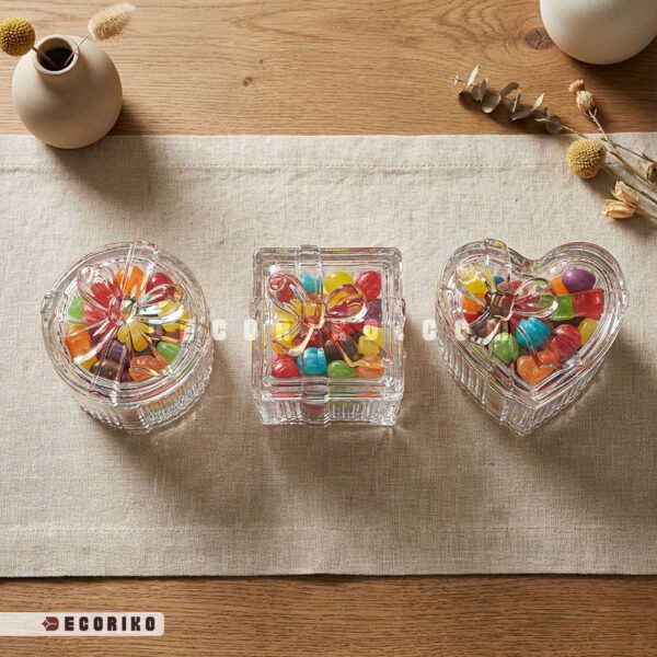 سه مدل قندان پر شده بلور طرح پاپیون در شکل‌های گرد، مربع و قلبی روی میز چوبی