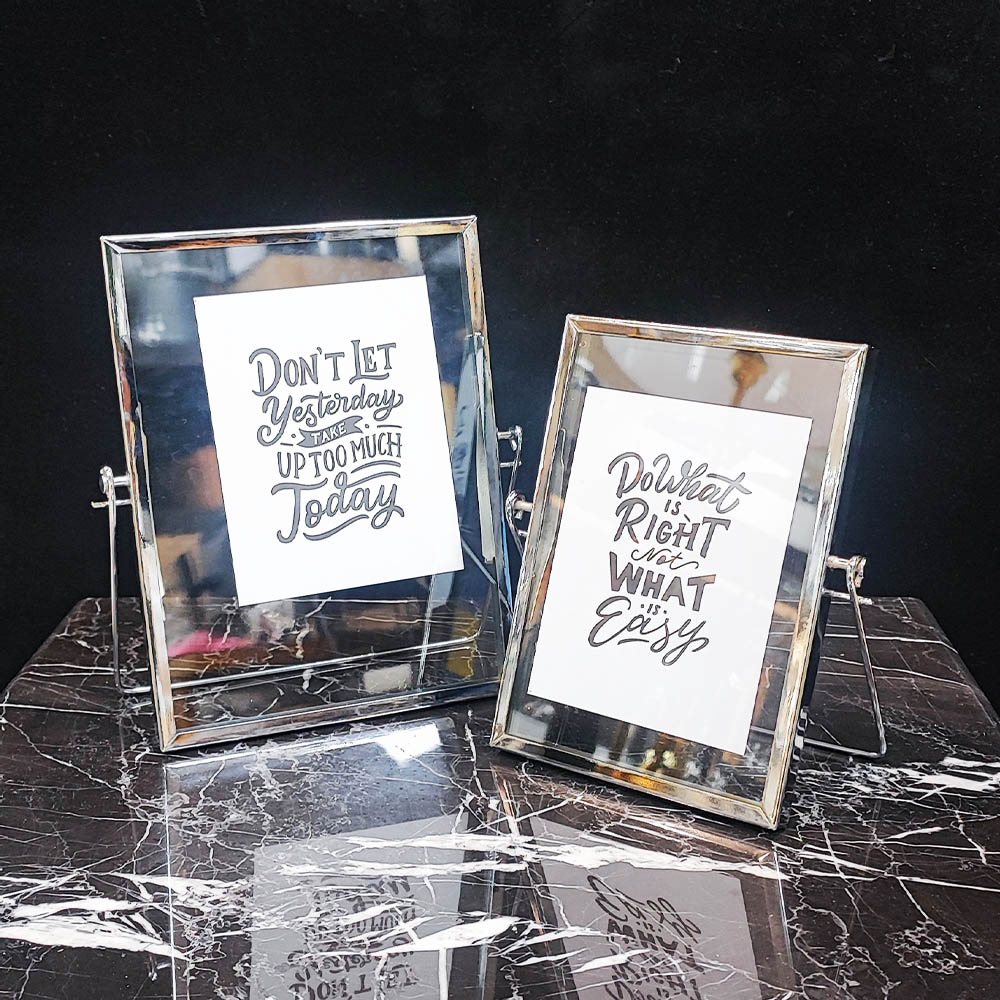 دو قاب عکس شیشه‌ای و فلزی نقره‌ای با پایه، مناسب دکوراسیون لوکس.