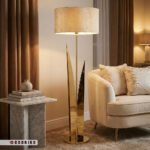 عکس ژورنالی آباژور ایستاده لوکس طلایی با نورپردازی گرم در کنار مبلمان راحتی