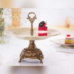 شیرینی خوری پایه دار آنتیک مدل ماربل با دسته فلزی و یک تکه کیک روی سینی